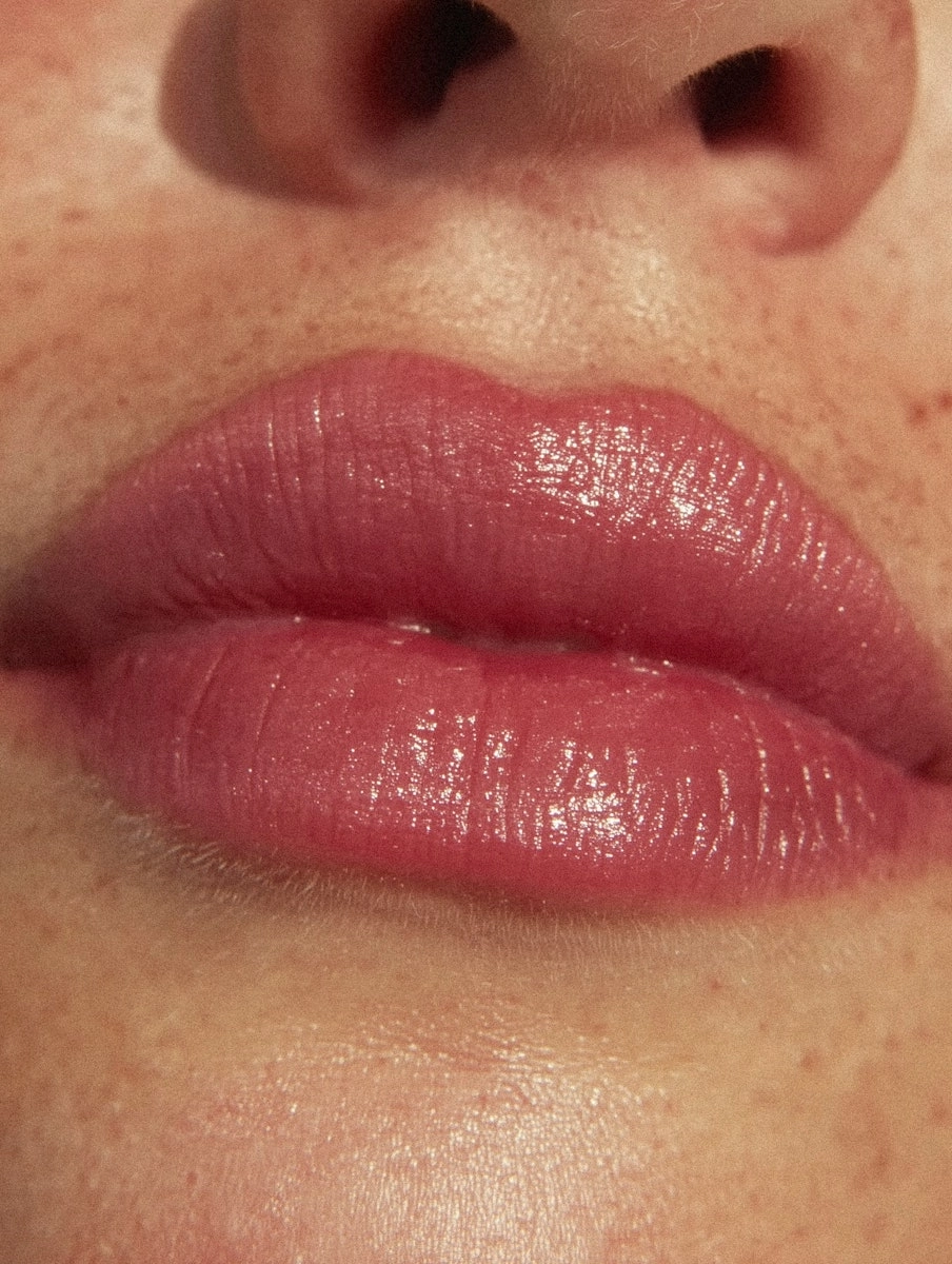 Close-up of glossy pink lips with natural skin texture and freckles